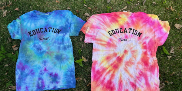 Two tie-dyed t-shirts on the grass, that read EDUCATION WASHU. One shirt is cool colorsm and one is warm colors.