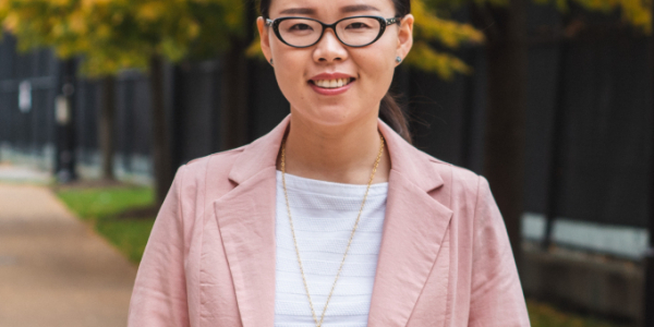 Yanjie Li photographed on Danforth Campus in the fall. She has dark hair, glasses, and a pink blazer.