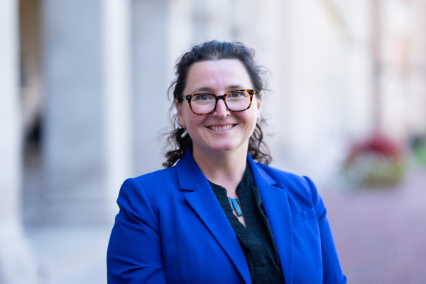 A white woman with curly brown hair and a bright blue blazer poses for a professional headshot.